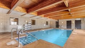 Piscina interna com teto de madeira, paredes azulejadas e área da piscina transparente.
