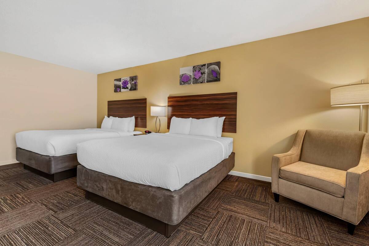 A hotel room with a double bed, two bedside tables, a chair, and a wall-mounted lamp.