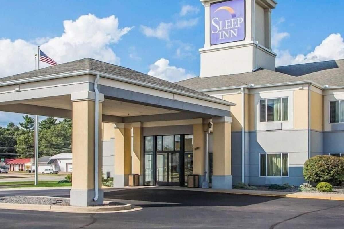 A Sleep Inn hotel with a covered entrance, a flag, and a clear sky.