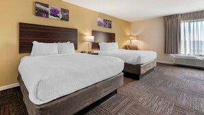 Quarto de hotel com duas camas, cabeceira de madeira, uma janela grande com cortinas e ar condicionado fixado na parede.