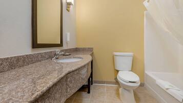A bathroom with a granite countertop, a white toilet, and a bathtub with a shower curtain.