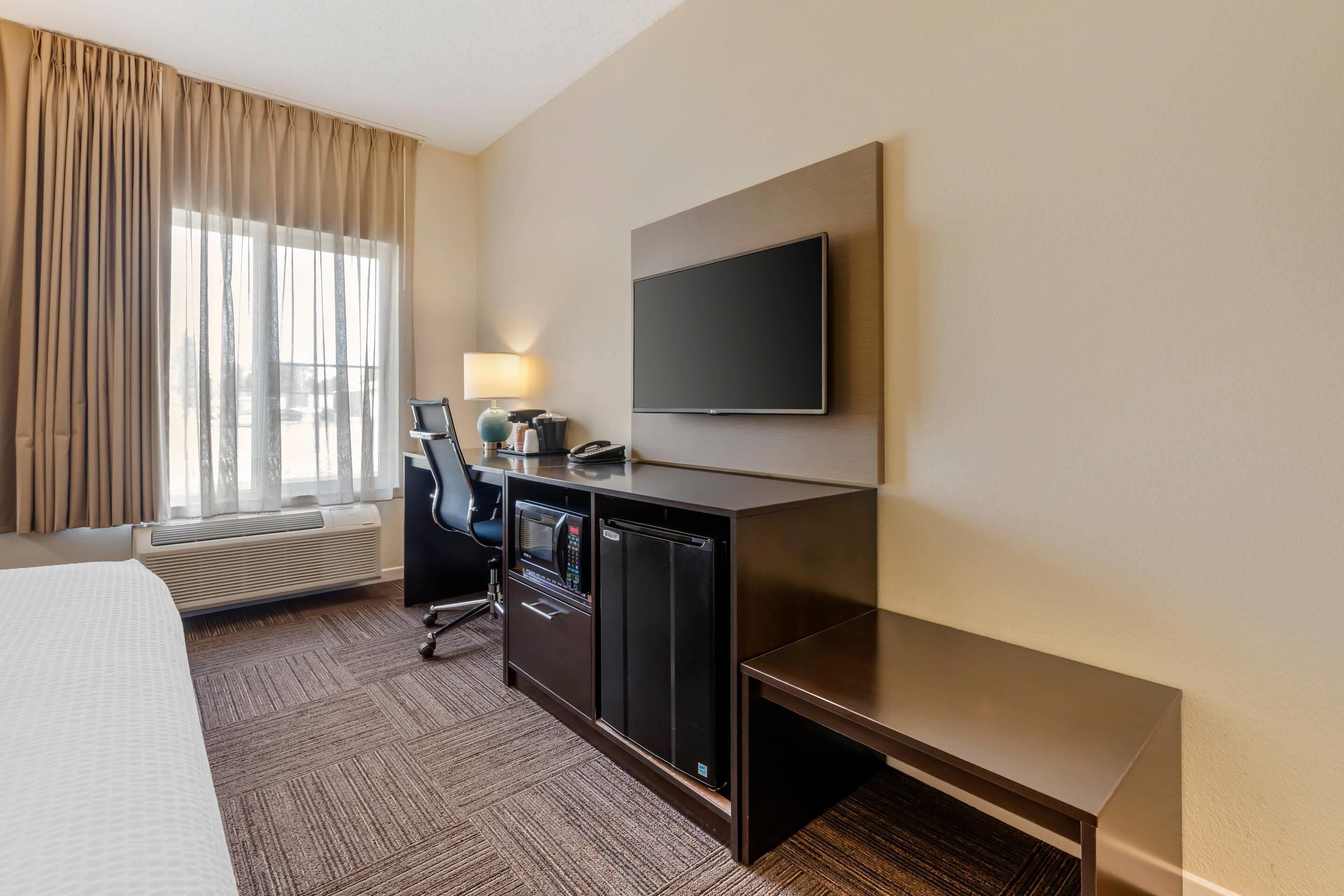 Hotelkamer met een bed, een bureau met een computer, een flatscreen televisie en een raam met gordijnen.