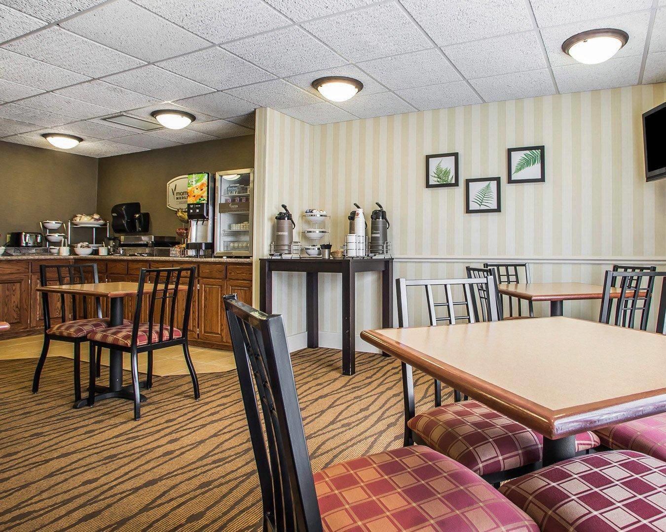 A hotel dining area with tables and chairs, a kitchen area, and a counter with various appliances.