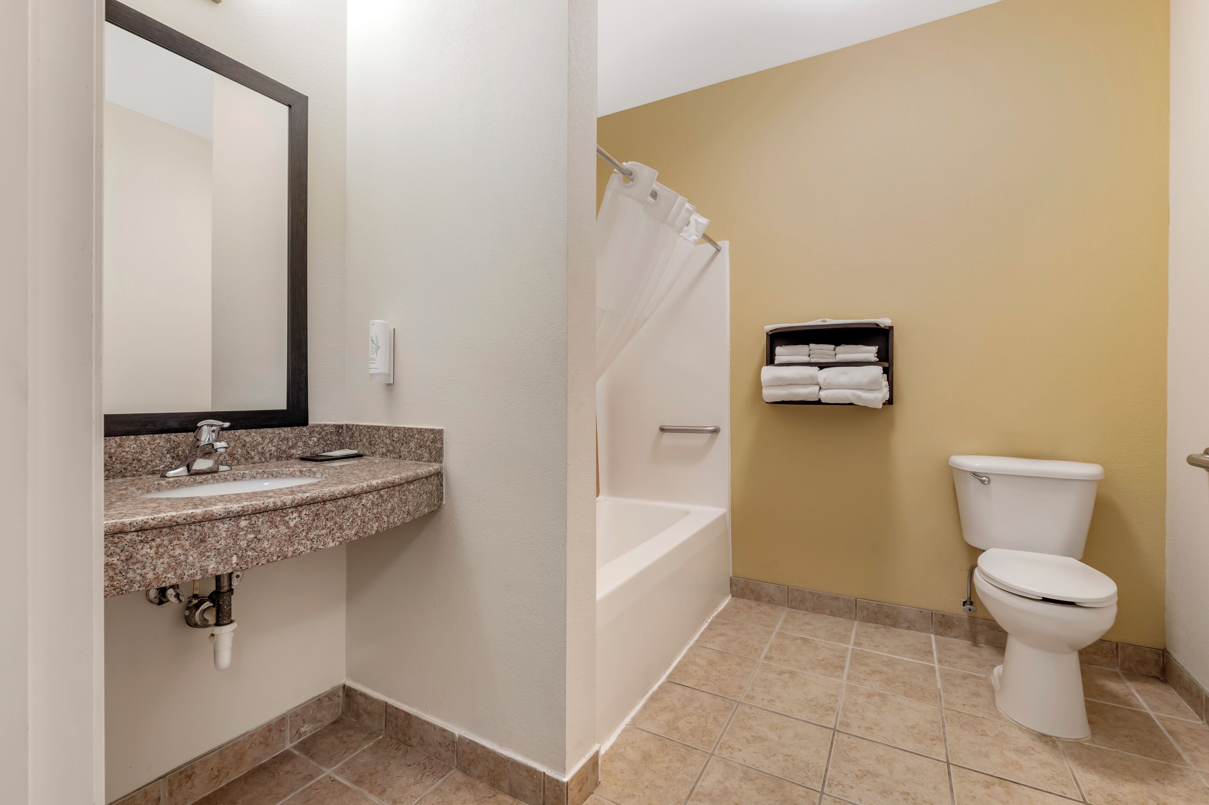 A bathroom with a granite sink, a white toilet, a bathtub, and a towel rack.