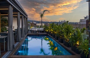 Piscina no terraço com vista para a cidade, rodeada por plantas em vasos e área de estar ao ar livre.