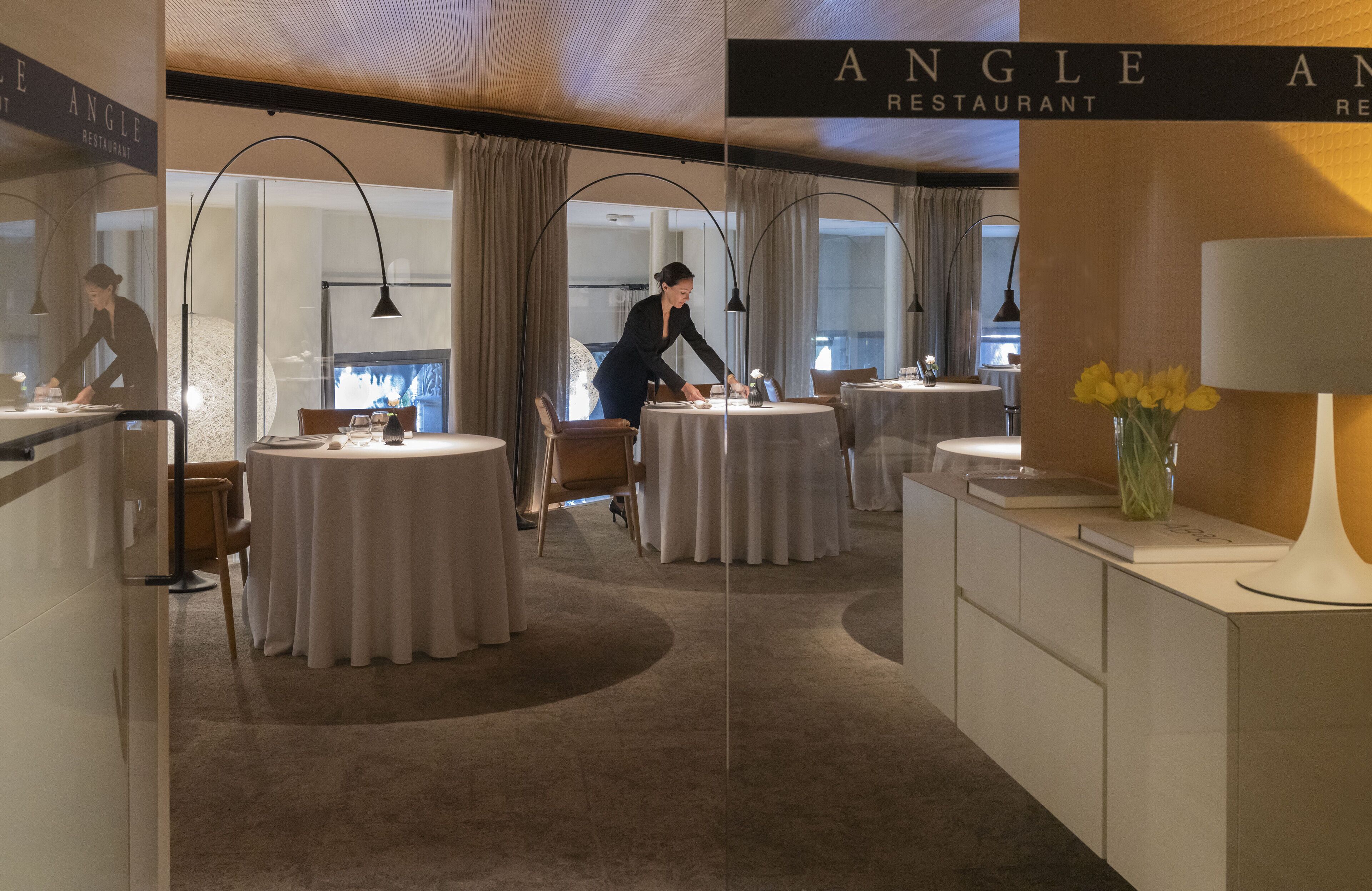 L’intérieur d’un restaurant avec des tables rondes, un bar et une vue par la fenêtre.