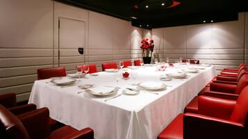 Une salle de conférence avec une longue table dressée pour un événement officiel, entourée de chaises rouges.