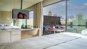 Una camera d'albergo moderna con un letto grande, una scrivania con un computer, una TV e un balcone con vista sulla città.
