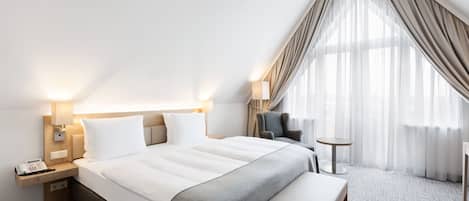 A modern hotel room with a large bed, bedside tables, a desk, and a chair.