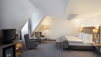 A modern hotel room with a large bed, a TV, a seating area with chairs, and a desk.