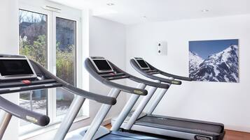 Une salle de sport équipée de tapis de course, dotée d’une grande fenêtre et ornée d’un tableau représentant une montagne.