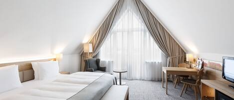 Una habitación de hotel con una cama grande, un escritorio, una silla, un televisor y una ventana con cortinas.