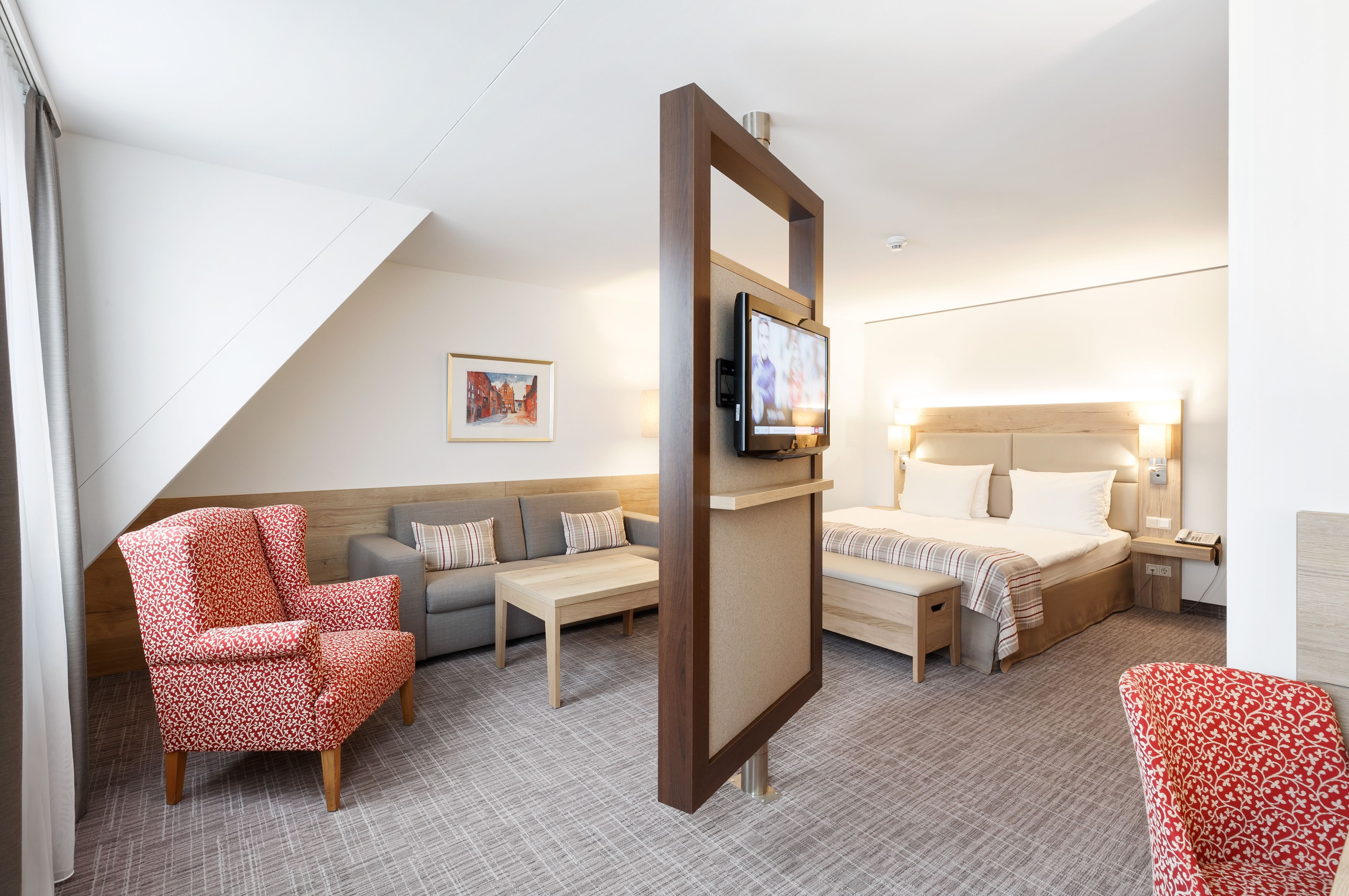 A hotel room with a sofa, armchair, bed, TV, and bedside table.