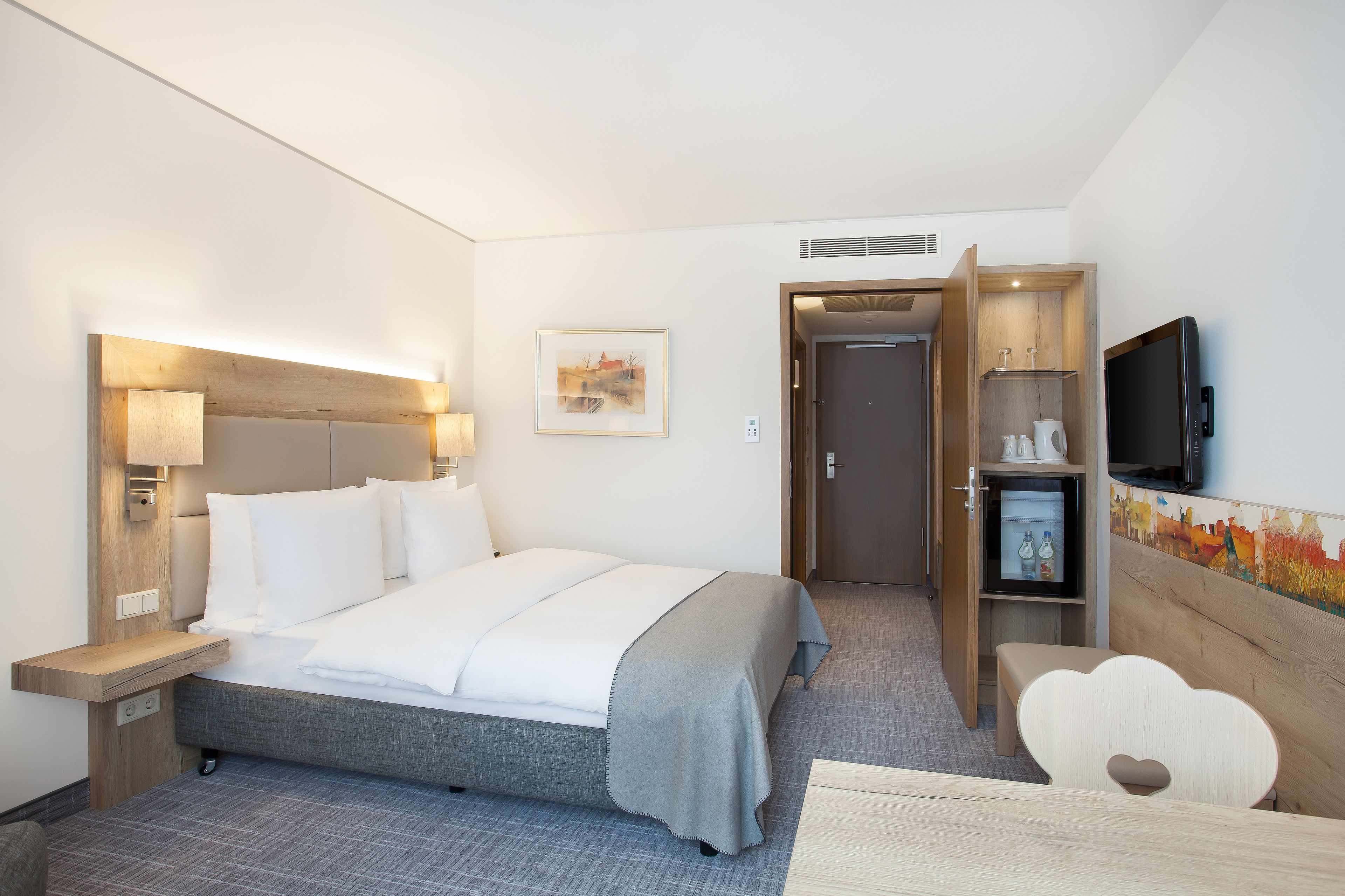 A hotel room with a bed, bedside table, lamp, TV, and a small cabinet.
