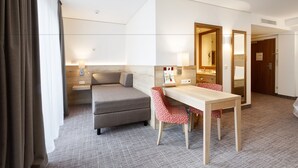 Et hotelværelse med seng, skrivebord, stol, spejl og dør til badeværelse.