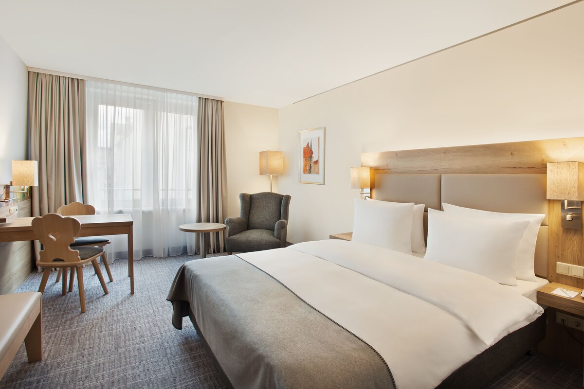 A hotel room with a bed, a desk, a chair, and a small table.