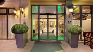 A hotel entrance with a glass door, a green mat, and two potted plants.