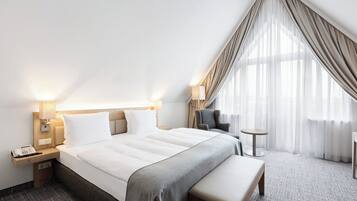 A hotel room with a large bed, bedside lamps, a small round table, a chair, and a bench.