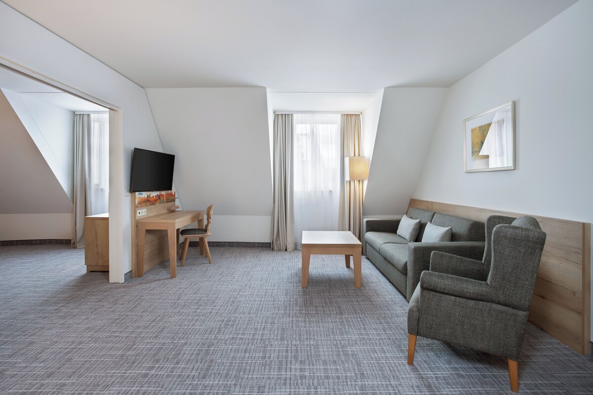 A hotel room with a desk, chair, sofa, and TV.