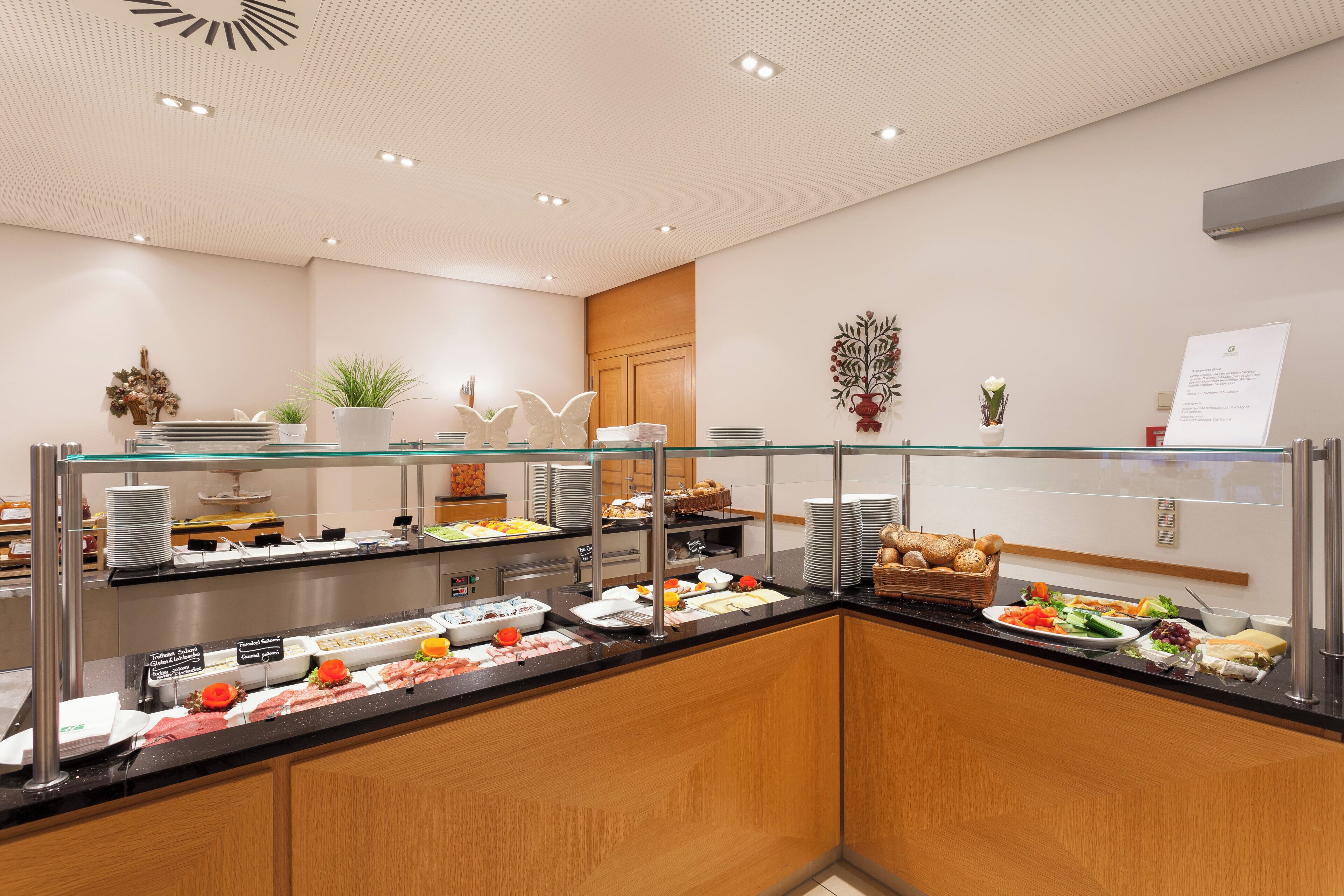 A buffet area with various food options, including salads, meats, and breads, with a glass partition and wooden cabinets.