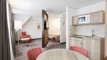 Ein Hotelzimmer mit Küchenzeile, einem Bett, einer Sitzecke mit Tisch und Stühlen sowie einem großen Fenster mit Vorhängen.