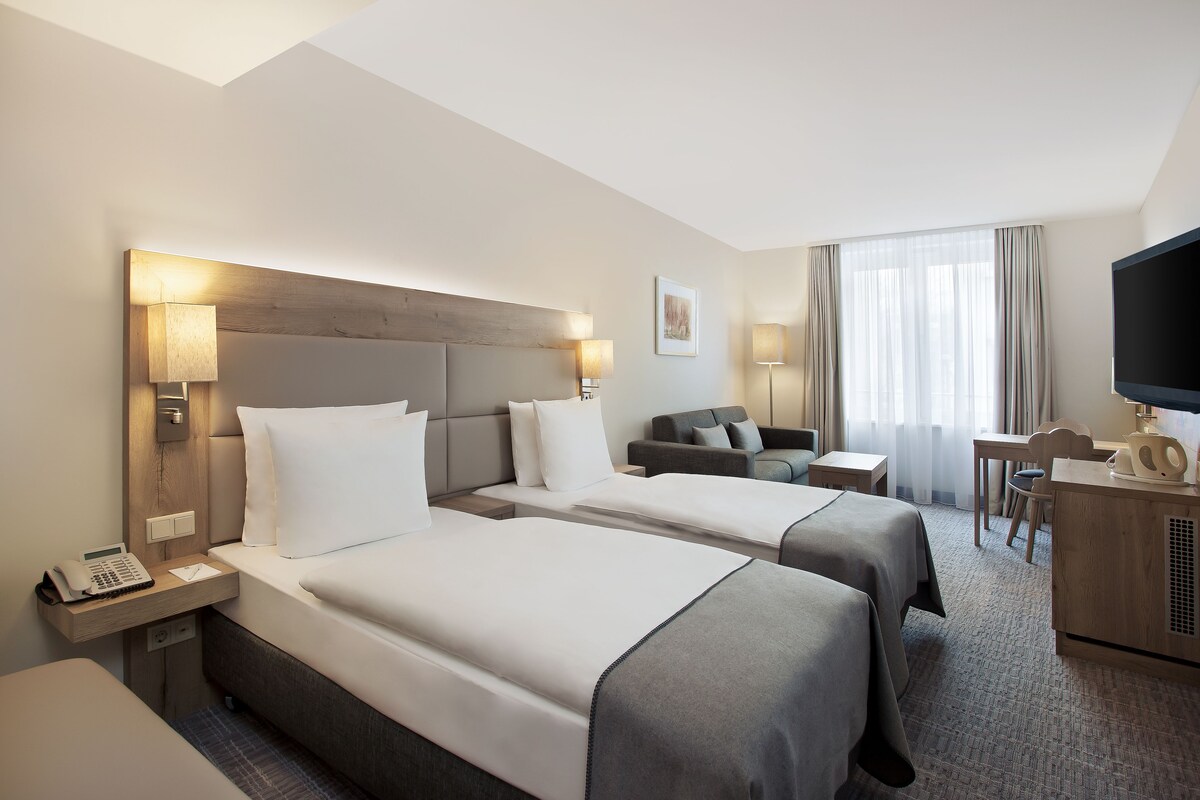 A hotel room with two beds, a desk, a television, and a sofa.