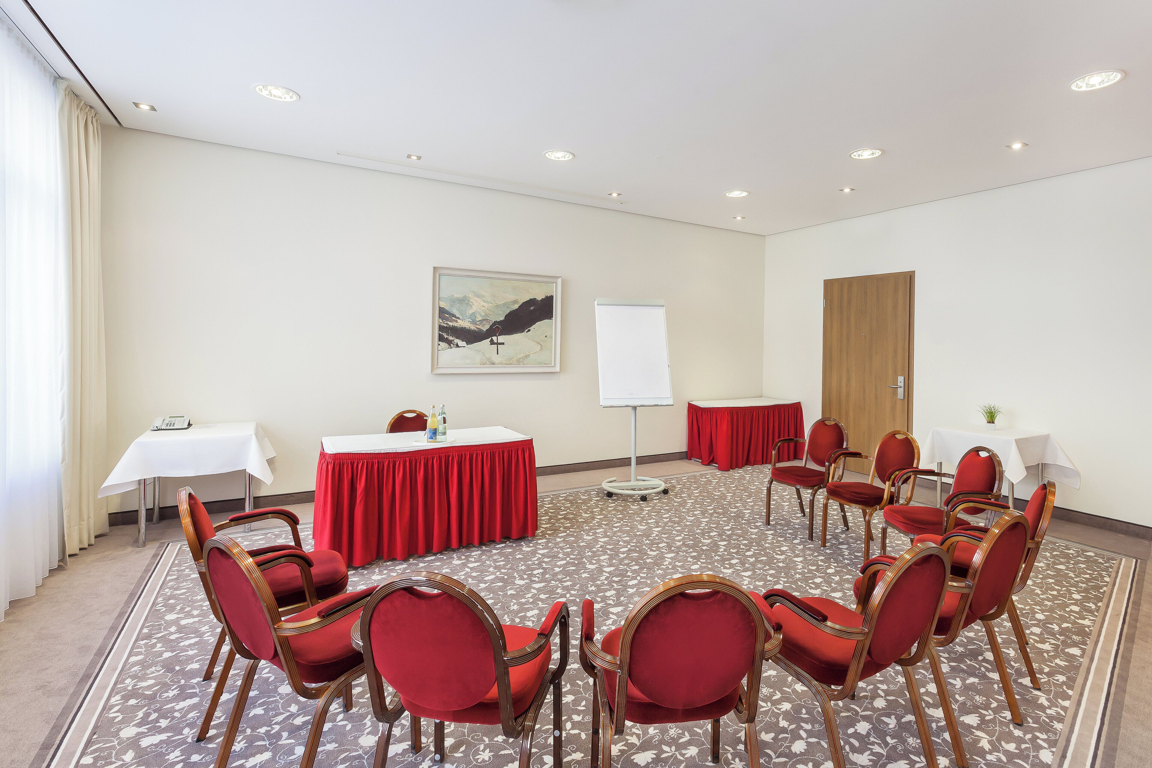 Una sala de conferencias con una mesa redonda, sillas rojas, una pizarra y un cuadro en la pared.