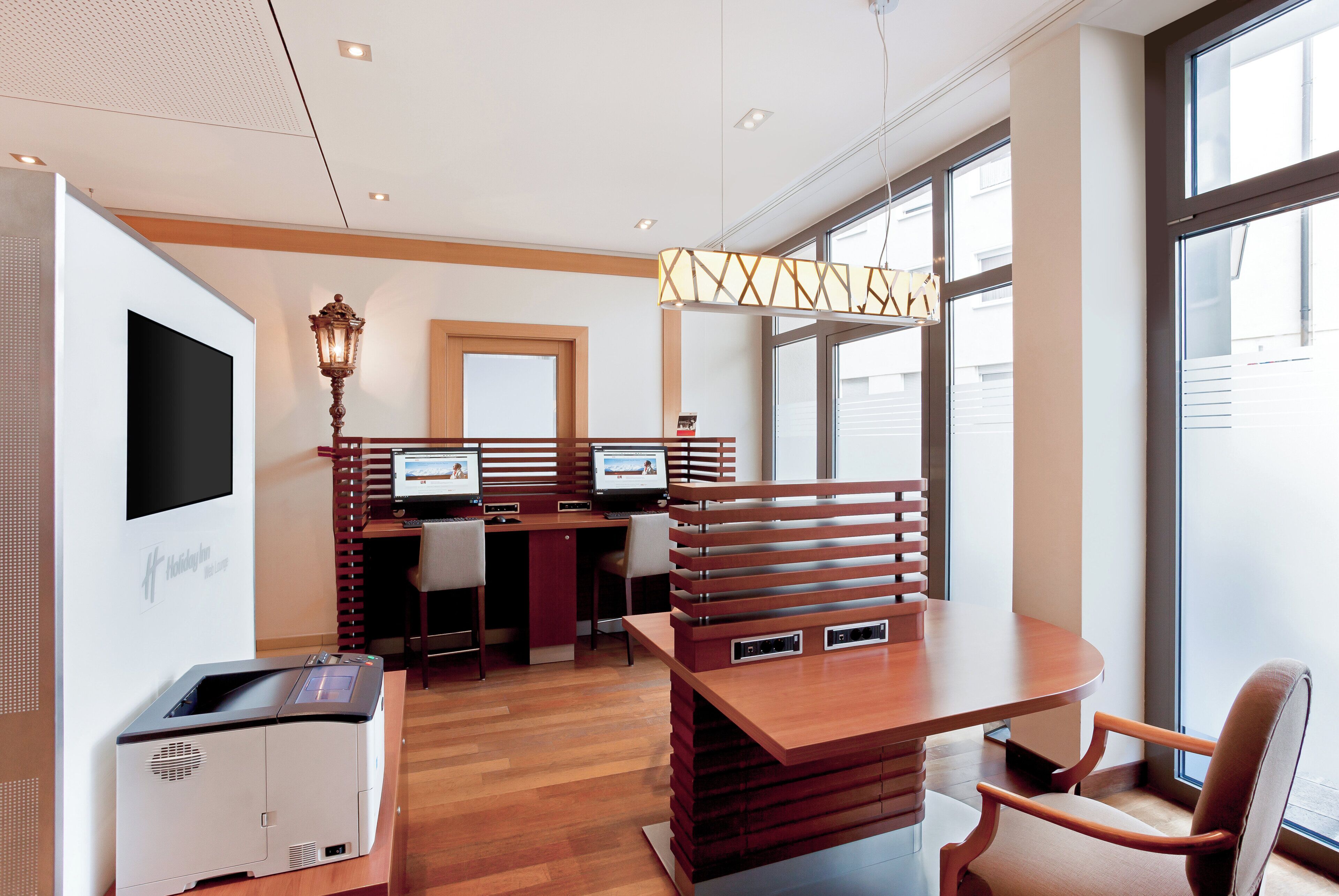 Habitación de hotel con escritorio, dos monitores, una impresora y un ventanal grande.