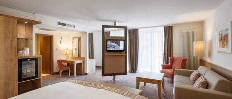 Una habitación de hotel con una cama grande, un escritorio, un televisor, un sofá y un minibar.