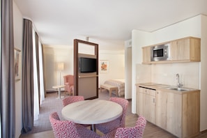 A compact hotel room with a dining area, a kitchenette, a bed, and a TV. - Holiday Inn Nürnberg City Centre by IHG (Nuremberg)
