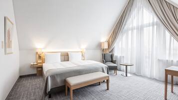 Una habitación de hotel con una cama grande, mesitas de noche, una silla, una pequeña mesa y un banco.