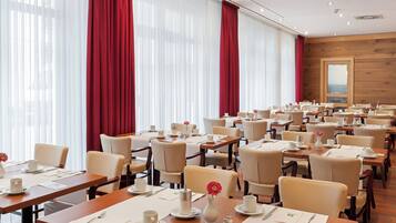 Comedor de hotel con varias mesas dispuestas para el desayuno, con manteles blancos, sillas y alimentos para el desayuno.