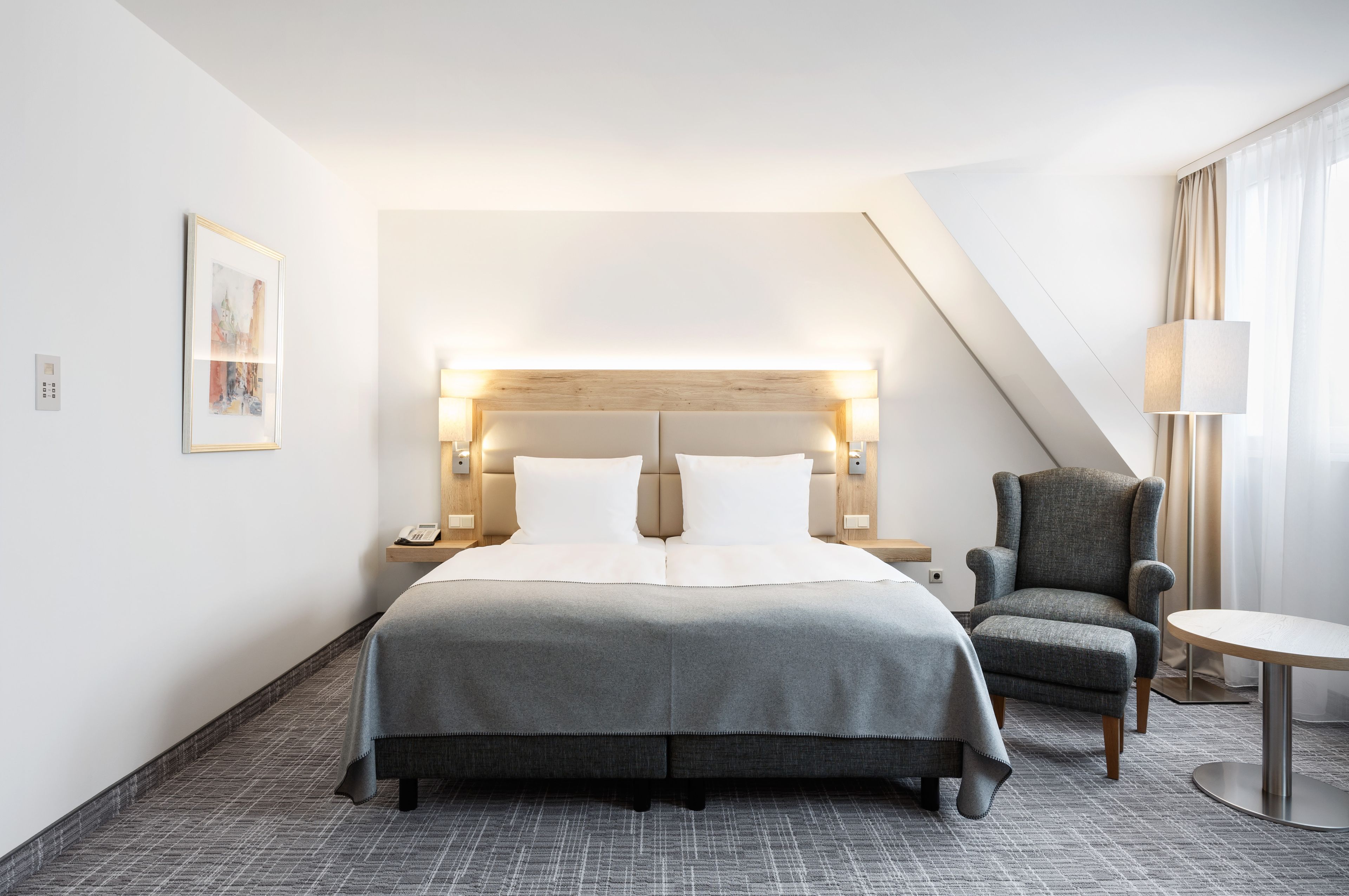 Une chambre d’hôtel avec un grand lit, une chaise, une petite table et une lampe.