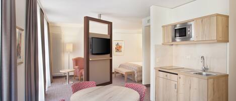 Habitación de hotel compacta con zona de comedor, kitchenette, televisor, cama y ventana con cortinas.