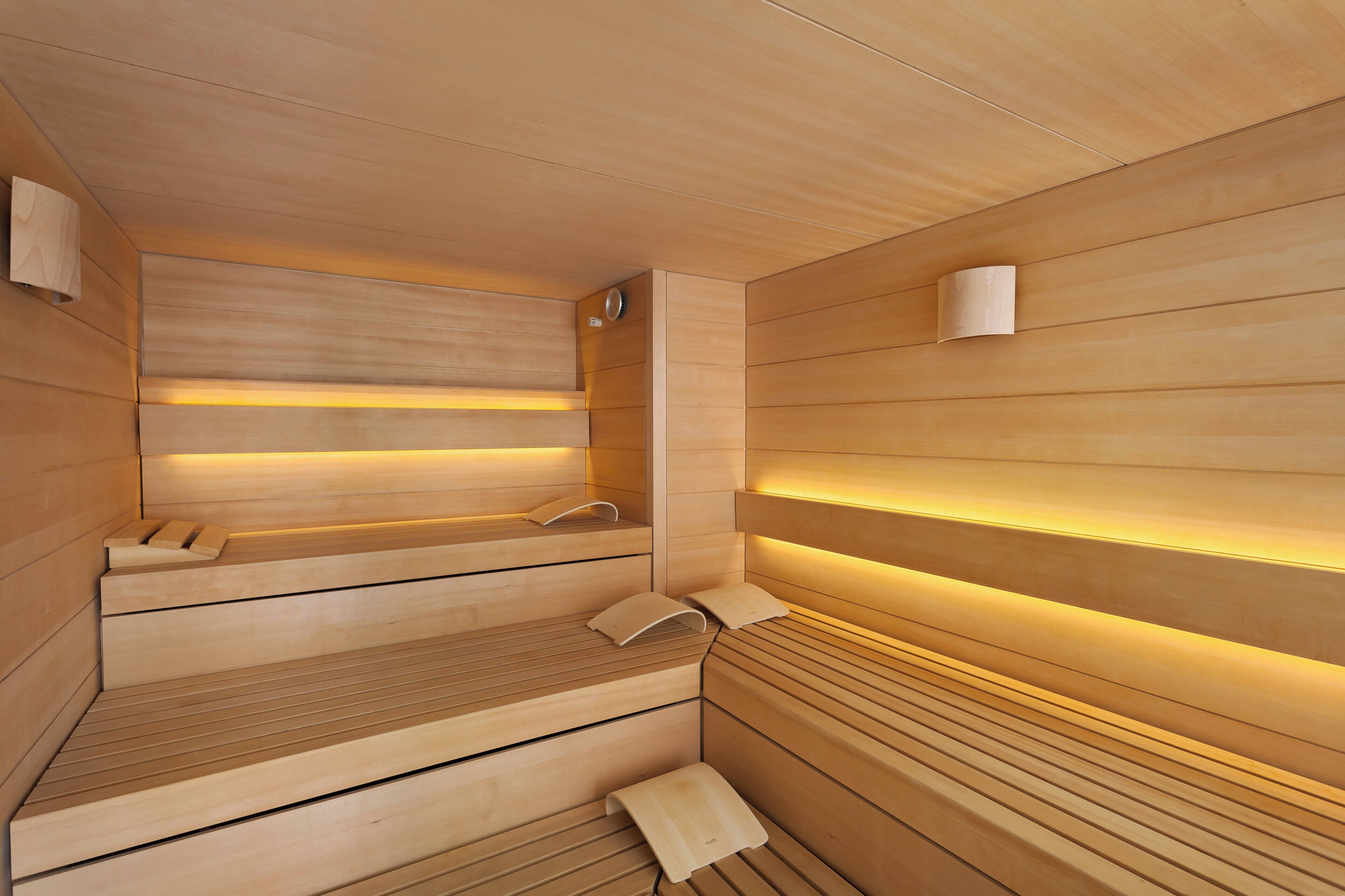 A sauna with wooden walls and benches, a towel rack, and a wall-mounted light fixture.