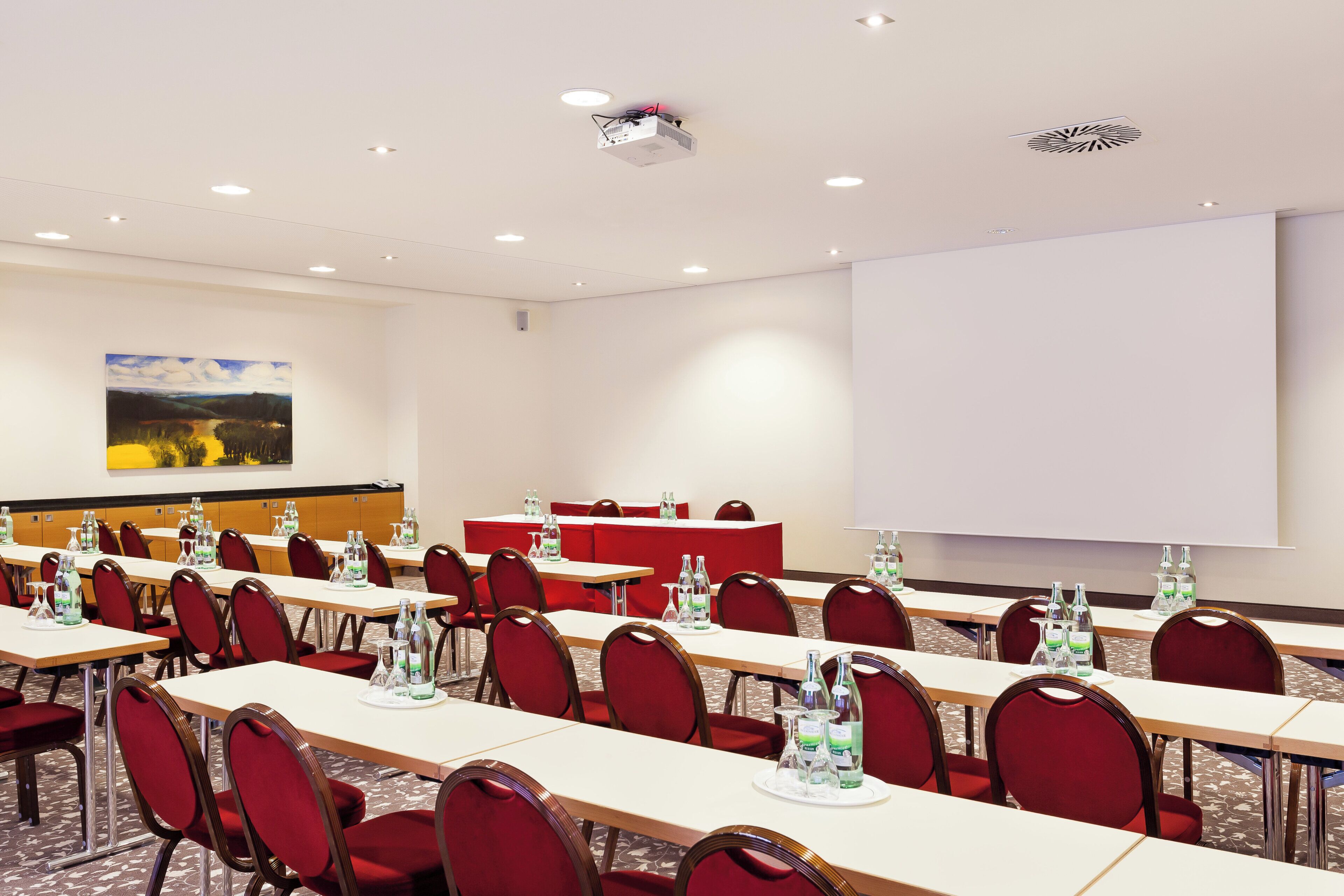 Une salle de conférence équipée de tables, de chaises et d’un écran de projection.