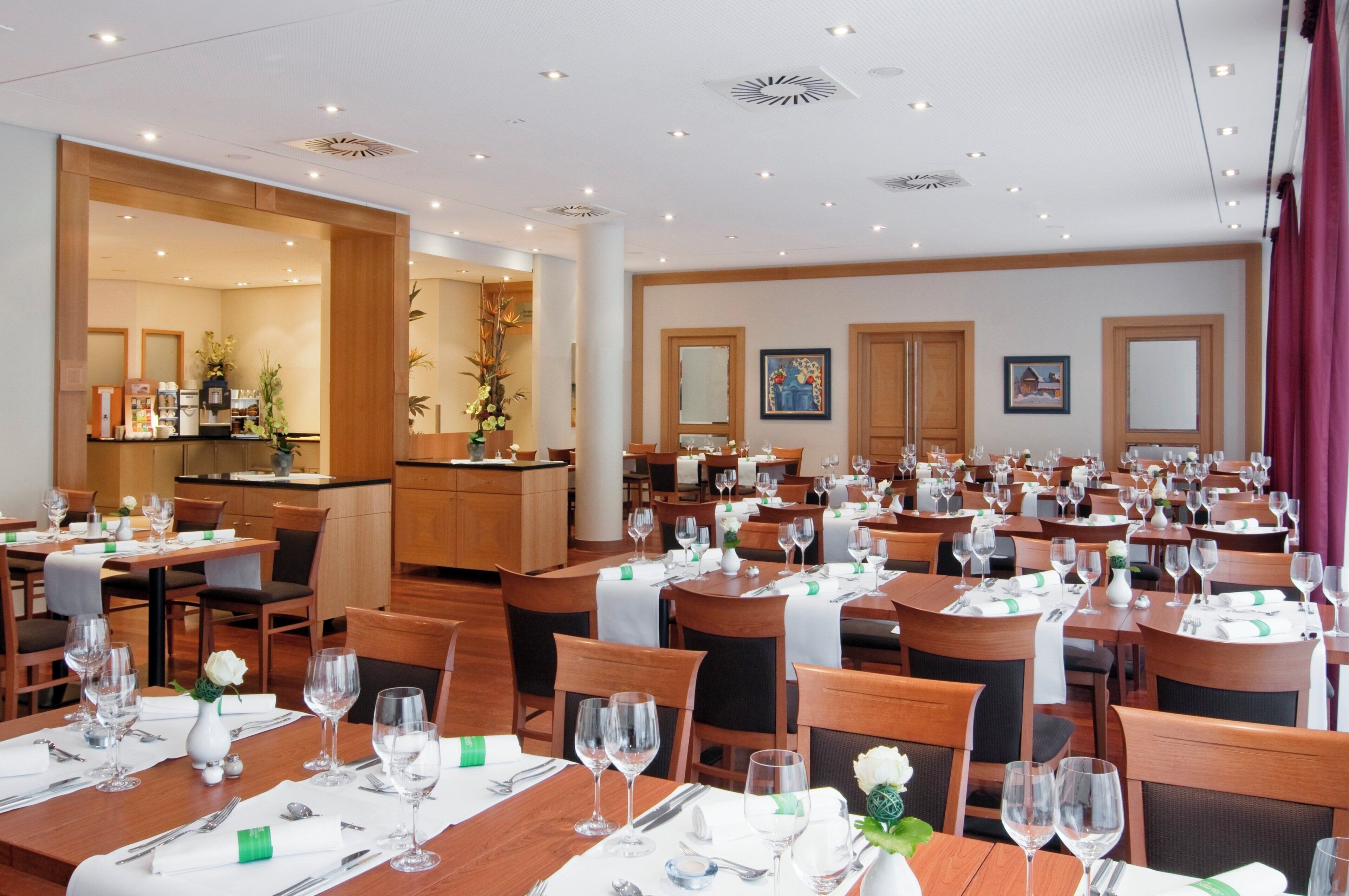 A hotel dining area with multiple tables set for guests, equipped with wine glasses, cutlery, and place settings.