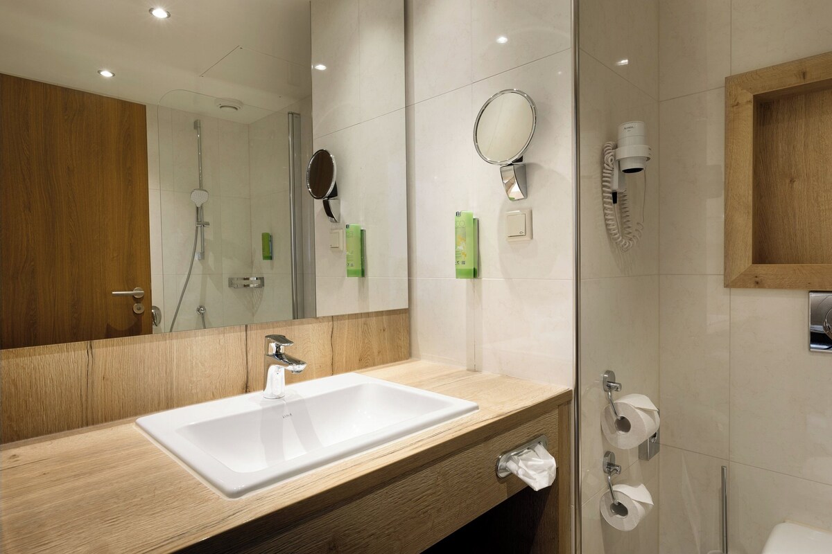 A modern bathroom with a wooden vanity, a white sink, a mirror, and a glass shower enclosure.