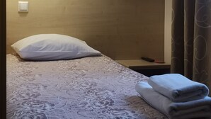 A hotel room with a bed, a white pillow, a folded towel, a nightstand, a remote control, and a painting on the wall. - Best Hotel (Riga)
