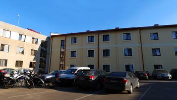 A parking lot with several cars and motorcycles, adjacent to a building with multiple windows and a flat roof.