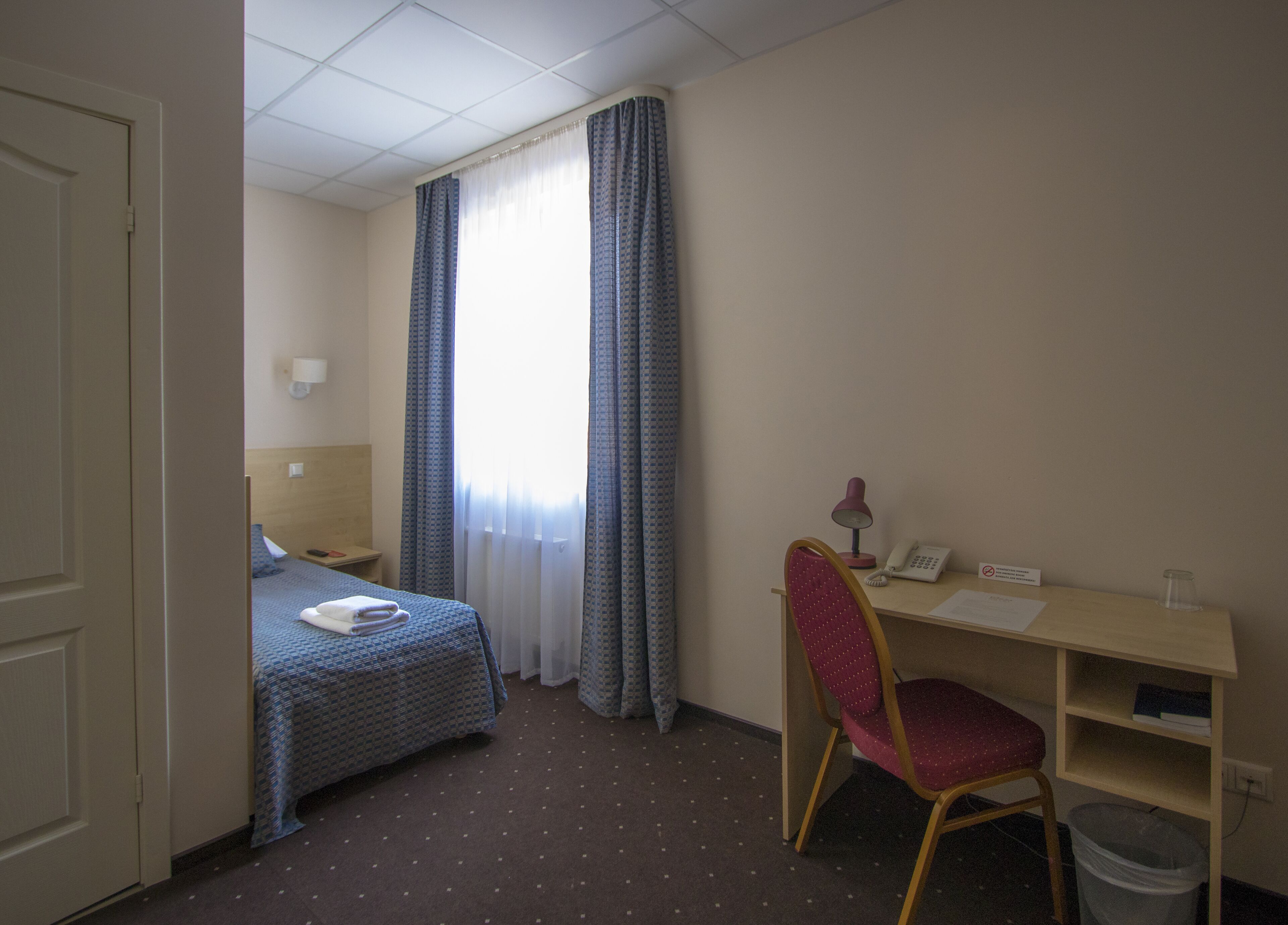 Hotellihuone, jossa on sänky, työpöytä tuolilla, puhelin ja roskakori.