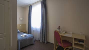 Hotellihuone, jossa on sänky, työpöytä tuolilla, puhelin ja roskakori.