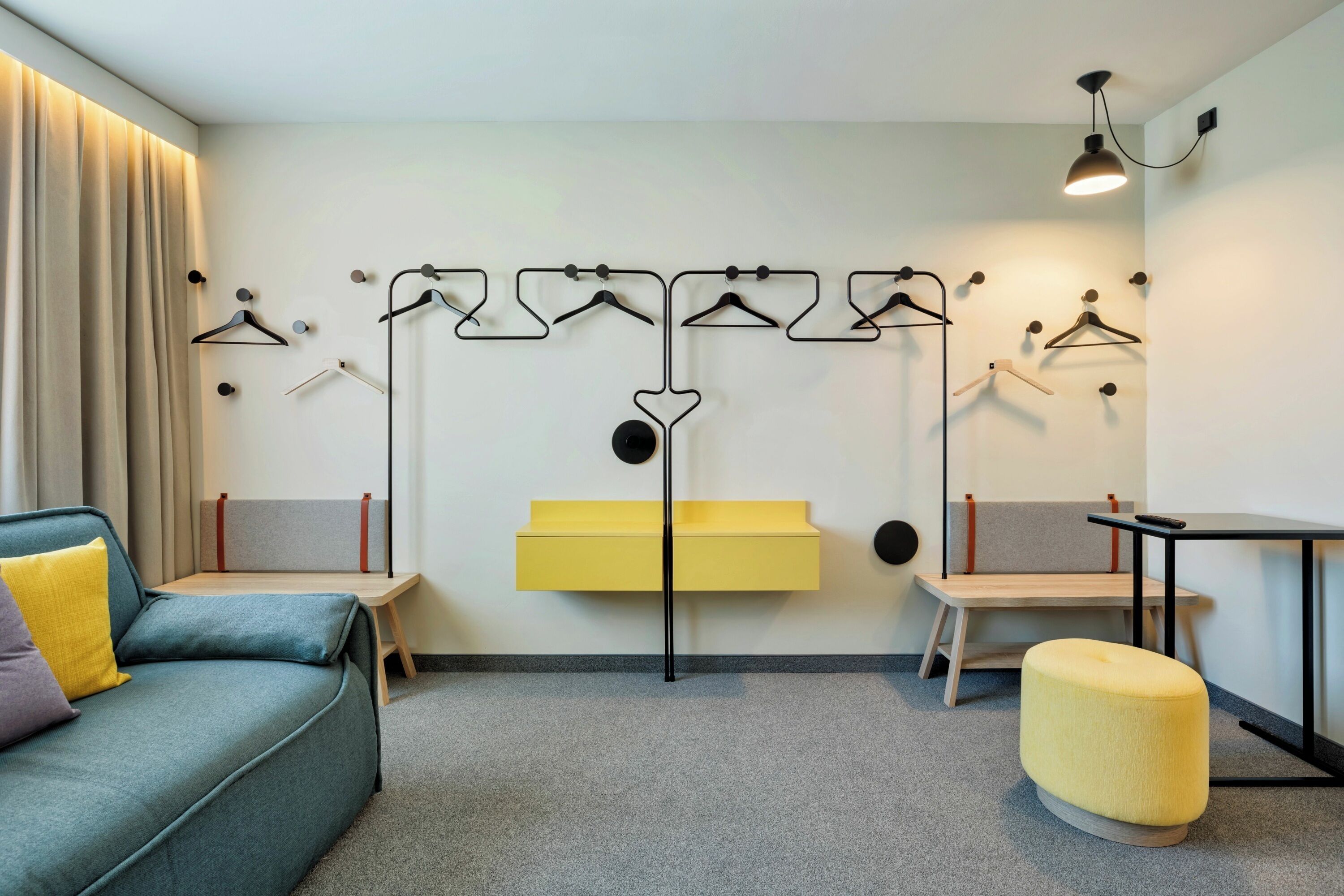 A modern hotel room with a sofa, ottoman, and a wall-mounted rack with multiple hangers.
