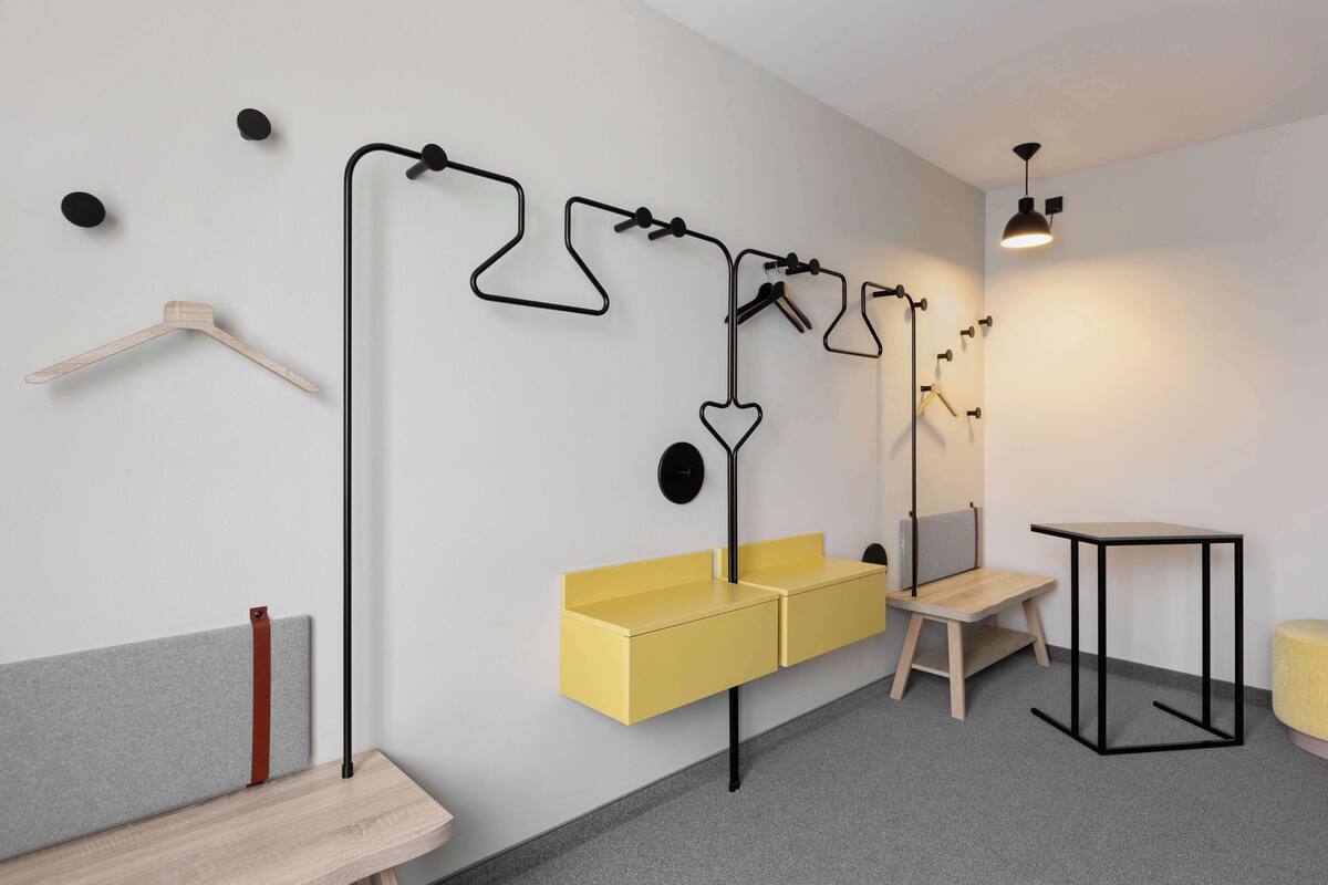 Ein modernes Zimmer mit einer hölzernen Bank, einer gelben Bank, einem kleinen Tisch und einer Pendelleuchte.