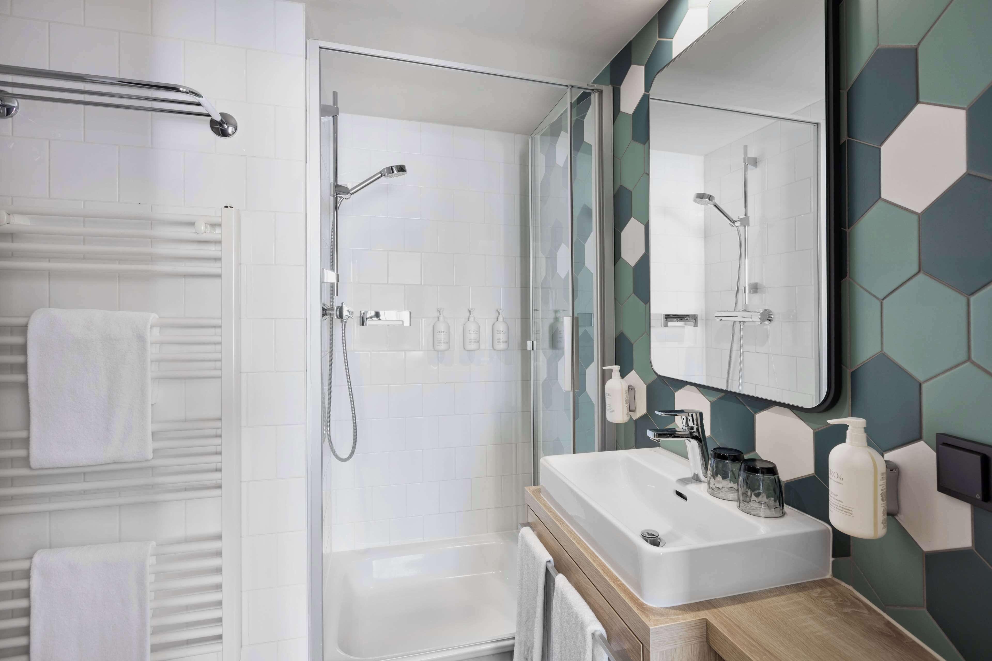 Ein modernes Badezimmer mit Duschabtrennung aus Glas, einem weißen Waschbecken mit Holzablage und einem Spiegel mit sechseckigem Fliesenrückwand.
