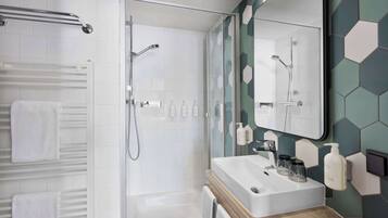 Ein modernes Badezimmer mit Duschabtrennung aus Glas, einem weißen Waschbecken mit Holzablage und einem Spiegel mit sechseckigem Fliesenrückwand.