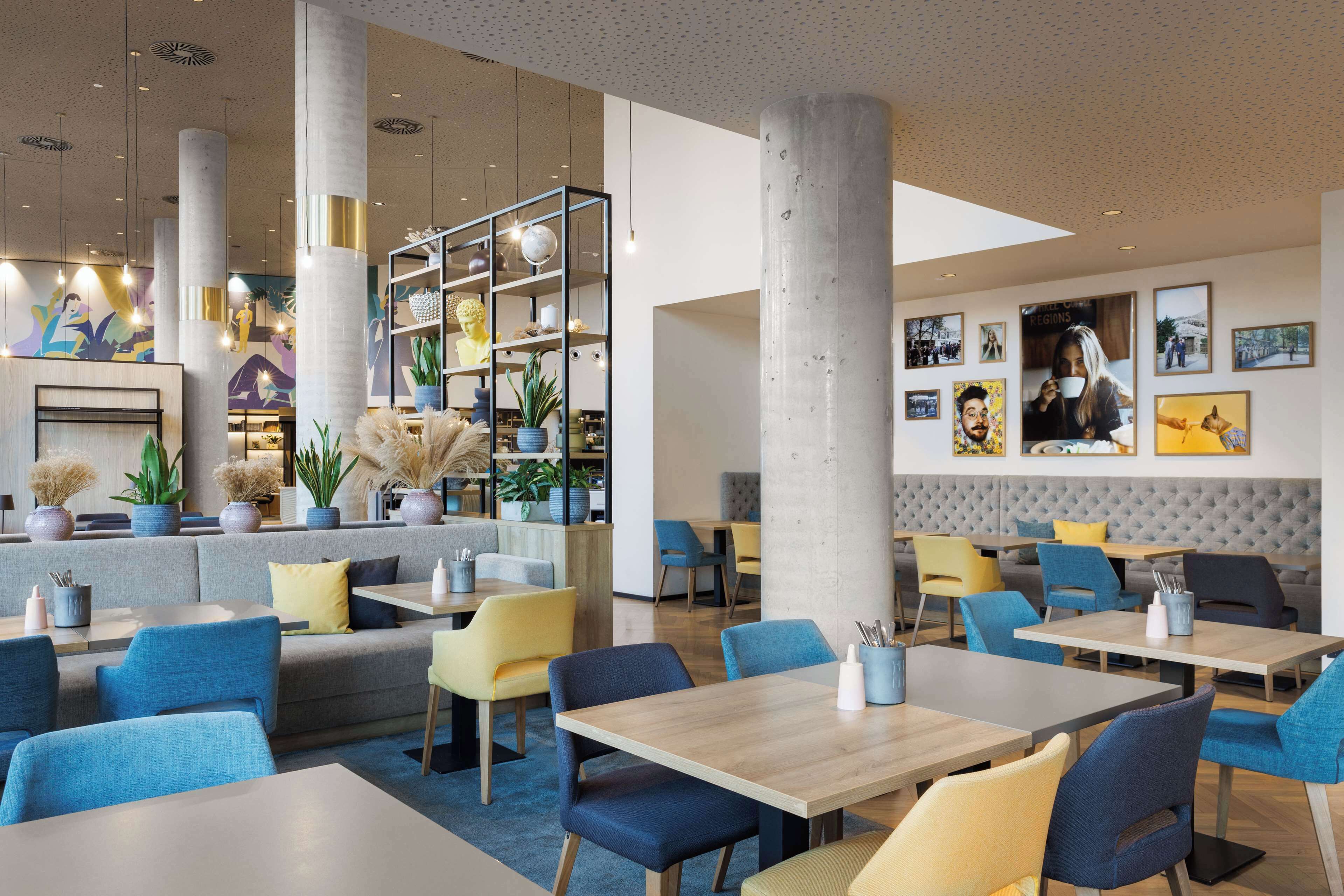 Ein modernes Restaurant mit hohen Decken, großen Fenstern und einer Mischung aus Sitzgelegenheiten, darunter Tische und gemütliche Sitzecken.