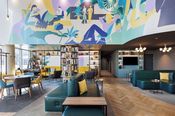 A modern library with green sofas, yellow cushions, and a large mural.