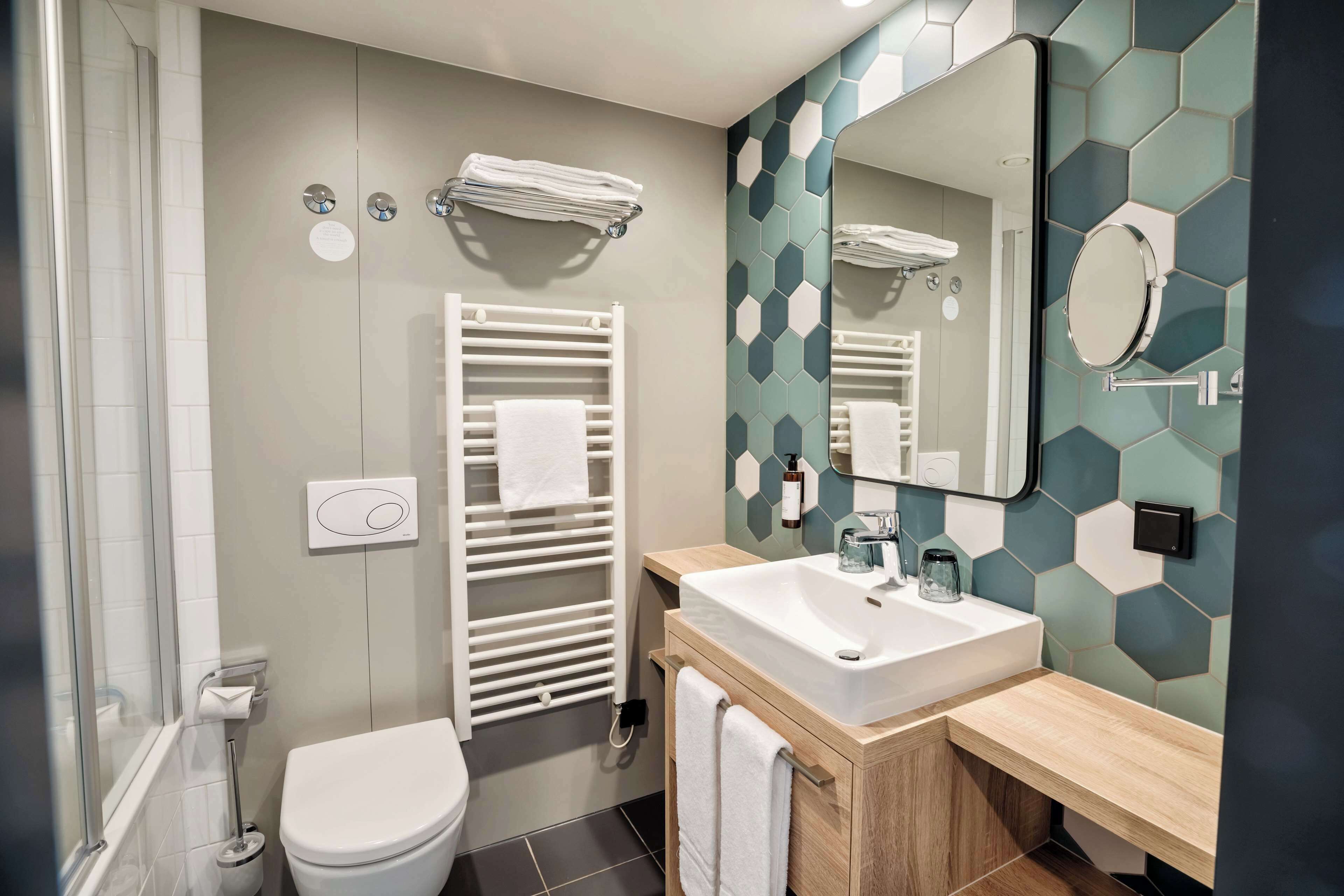 A modern bathroom with a white toilet, a white towel rack, a sink with a mirror, and a shower area.