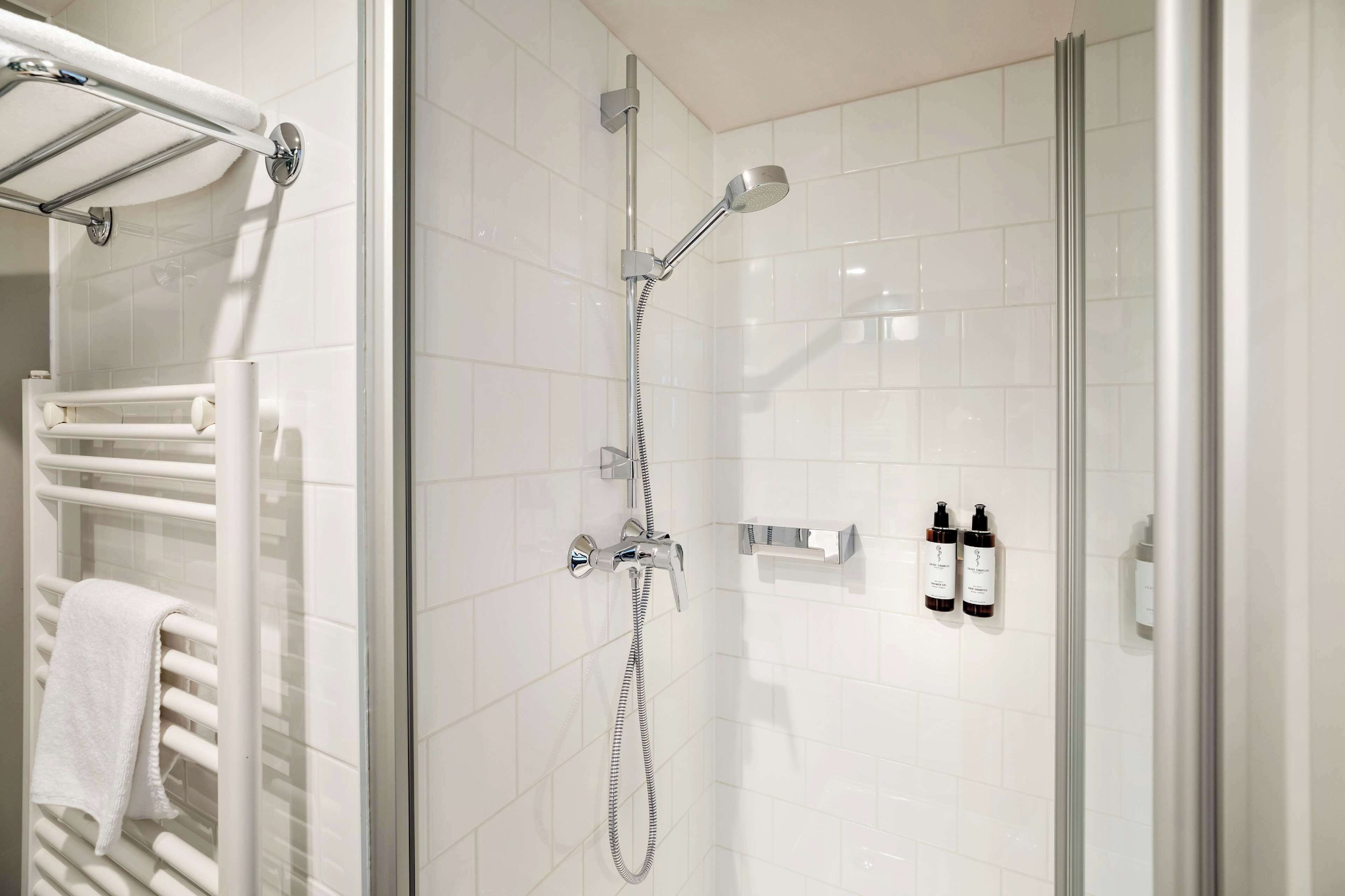 Un baño moderno con ducha de vidrio, toallero blanco y dos botellas de champú en la pared.